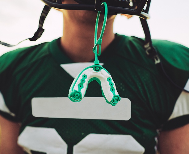 Teen with athletic sportsguard hanging from football helmet