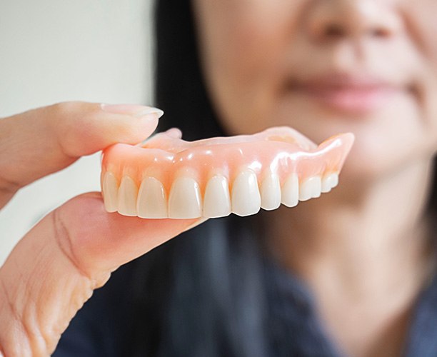 Dentist holding upper arch of dentures with thumb and forefinger