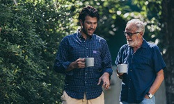 Two men outside walking and talking with coffee