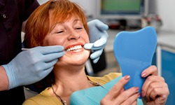 Woman with red hair smiling at reflection as dentist pokes her teeth