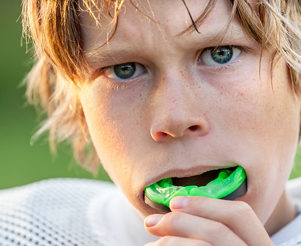 Teen boy placing green athletic mouthguard