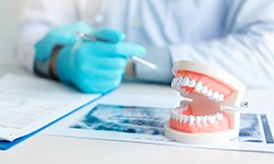 Dentist in blue gloves looking over patient’s chart with toy teeth on the desk