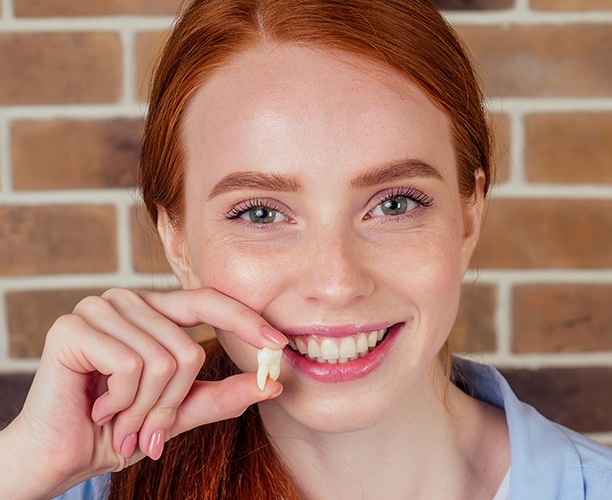 Woman holding up a tooth to her smile after tooth extractions