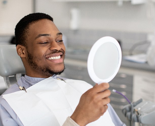 Man smiling while looking at reflection in handheld mirror