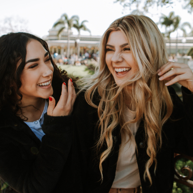 Two young women laughing together with palm trees in background