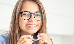young girl with glasses holding an Invisalign aligner 