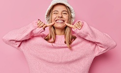 Woman in pink sweater pointing to her smile