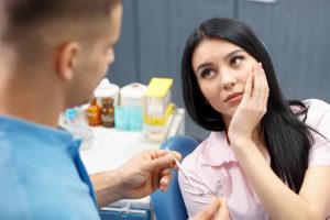 woman holding her mouth in pain while talking to dentist