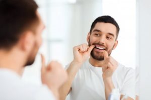 Man looking in the mirror flossing his teeth