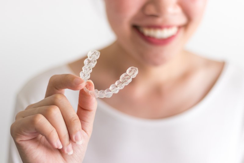 person holding Invisalign aligner tray and smiling