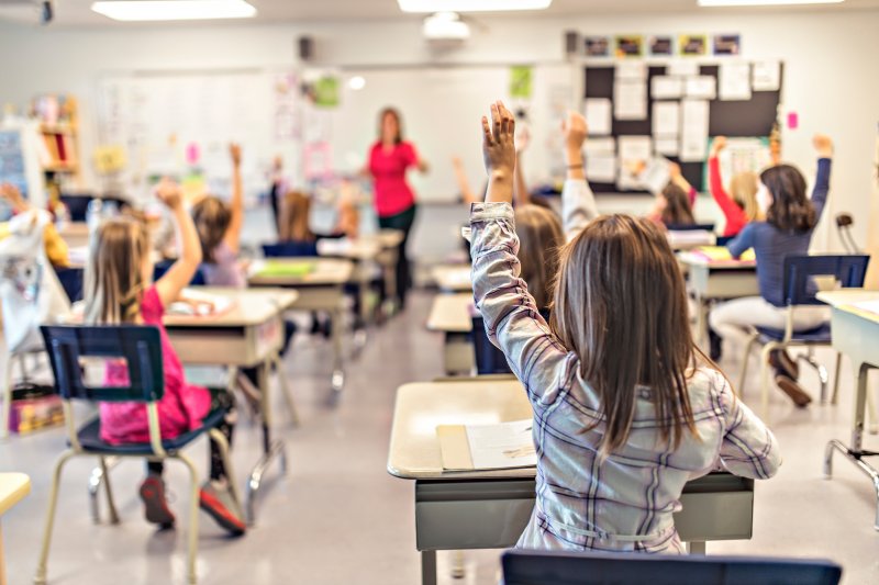 A group of children raising their hands in school