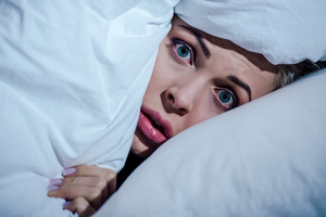Scared woman peeking out from below some pillows